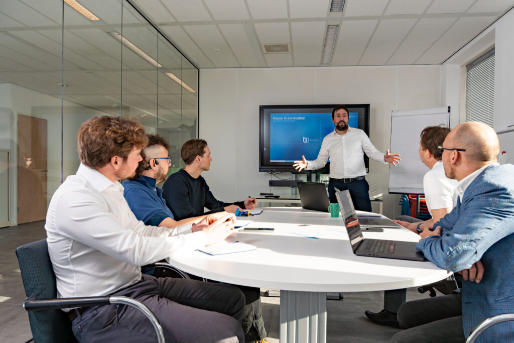 Bluem team gathered around a meeting table while a colleague presents on a screen